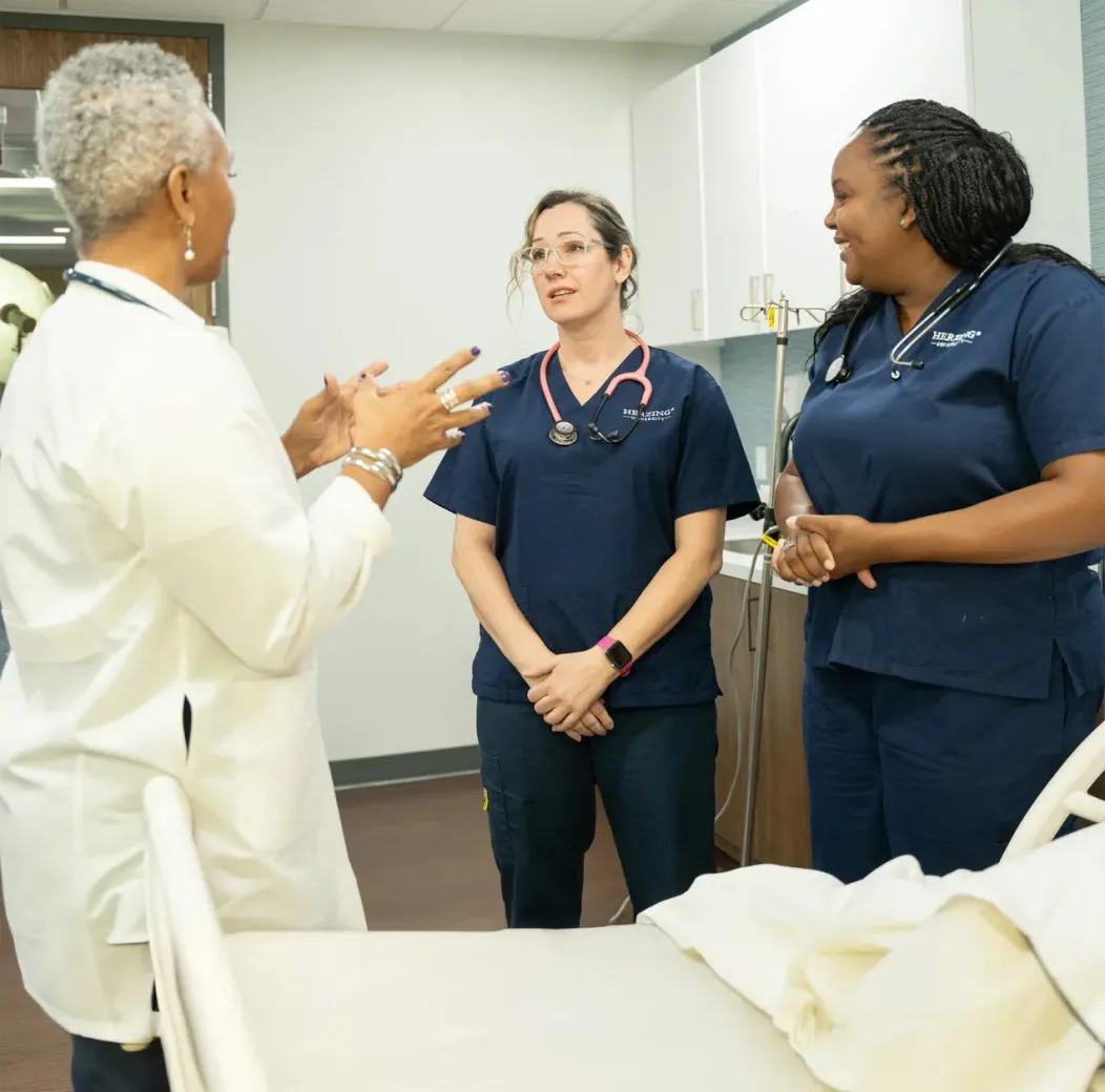 Nursing educator speaking with two students in scrubs during a clinical training session, fostering discussion and mentorship in a healthcare education setting.